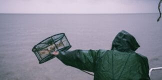 Wędkarz w płaszczu przeciwdeszczowym zarzuca sieć na morzu podczas deszczu