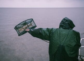 Wędkarz w płaszczu przeciwdeszczowym zarzuca sieć na morzu podczas deszczu